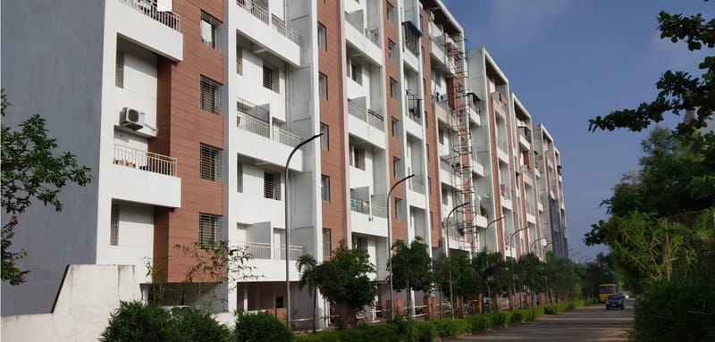 MH14 Talegaon — photograph of a completed and occupied residential block, four storeys of white and terracotta-panelled flats with projecting balconies, along a landscaped street.
