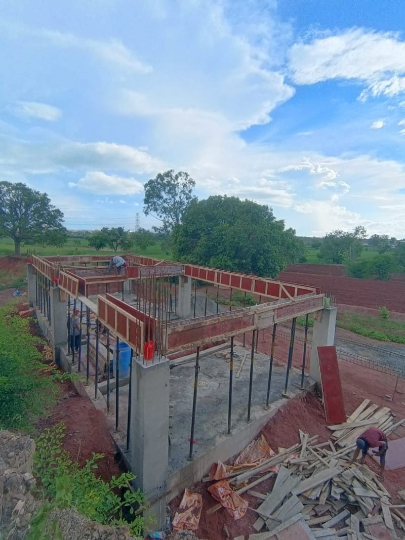 Nikita Textiles, Textile Park, Borgaon — site photograph looking along the shuttered plinth beams, with workers fixing formwork and stacked shuttering boards in the foreground.