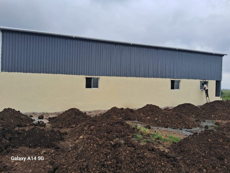 Textile industry shed for Shri Sai Textiles, Kanagala Industrial Area, KIADB — site photograph of the long side elevation, showing the full run of metal cladding above a cream plinth wall with evenly spaced windows.